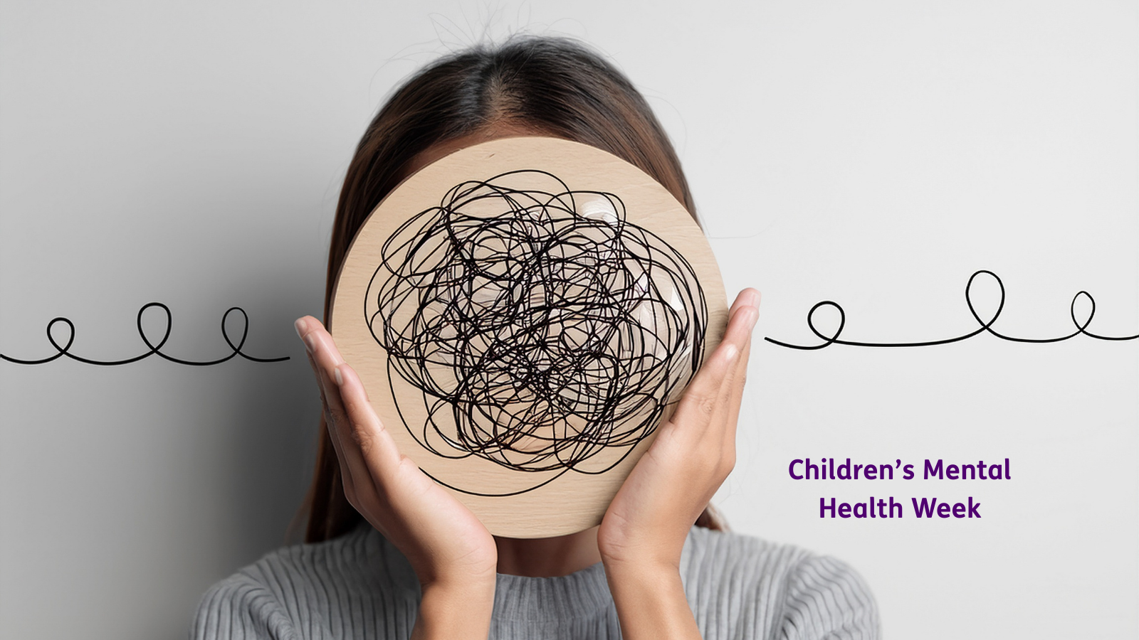 Graphic for Children’s Mental Health Week showing a person holding a round wooden board in front of their face, covered in tangled black scribble lines, with a single line looping across the background. Purple text on the right reads “Children’s Mental Health Week.”Graphic for Children’s Mental Health Week showing a person holding a round wooden board in front of their face, covered in tangled black scribble lines, with a single line looping across the background. Purple text on the right reads “Children’s Mental Health Week.”