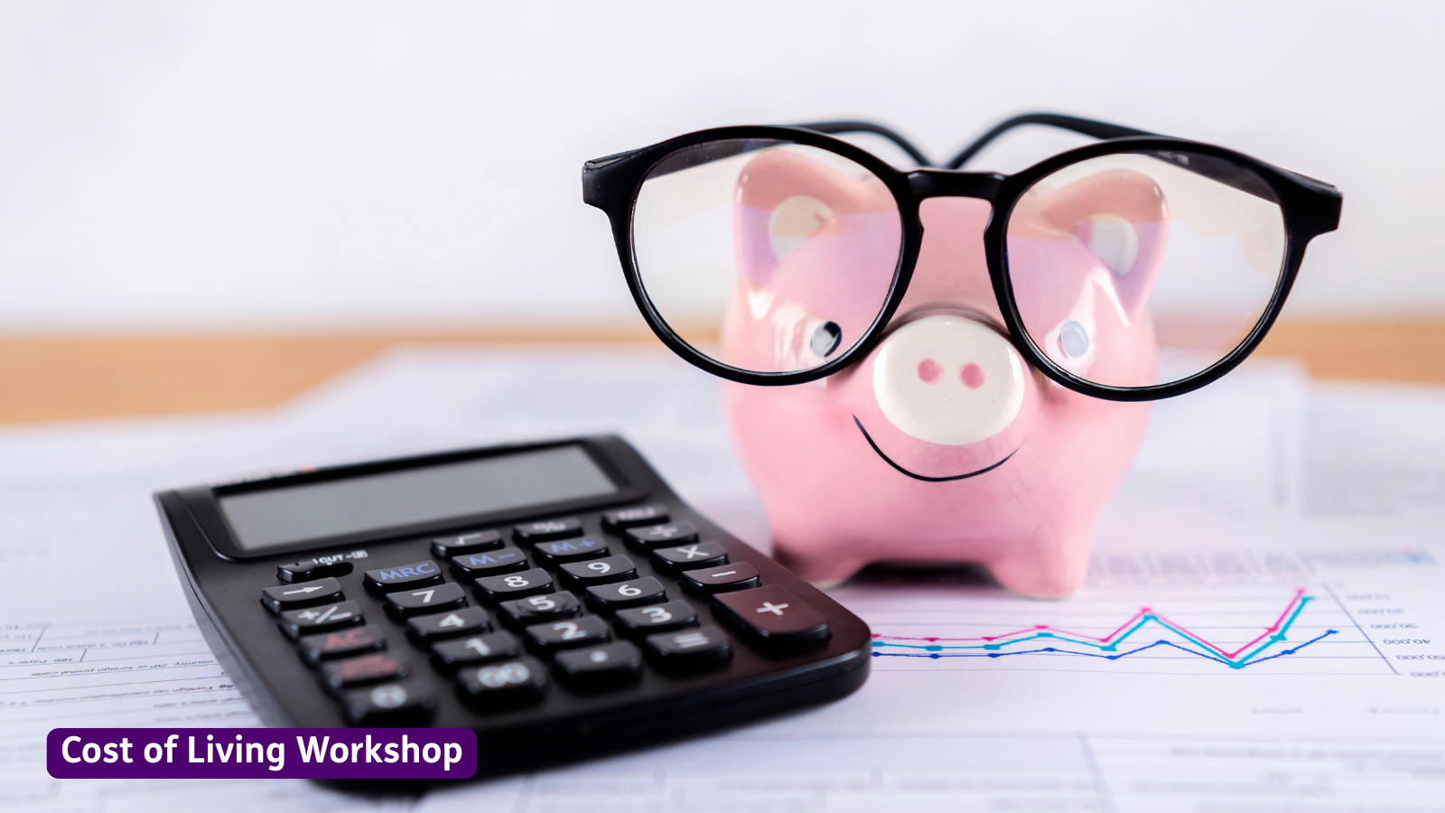 Photo of a calculator on paperwork with a line graph, beside a pink piggy bank wearing black glasses. A purple label at the bottom left reads “Cost of Living Workshop.”